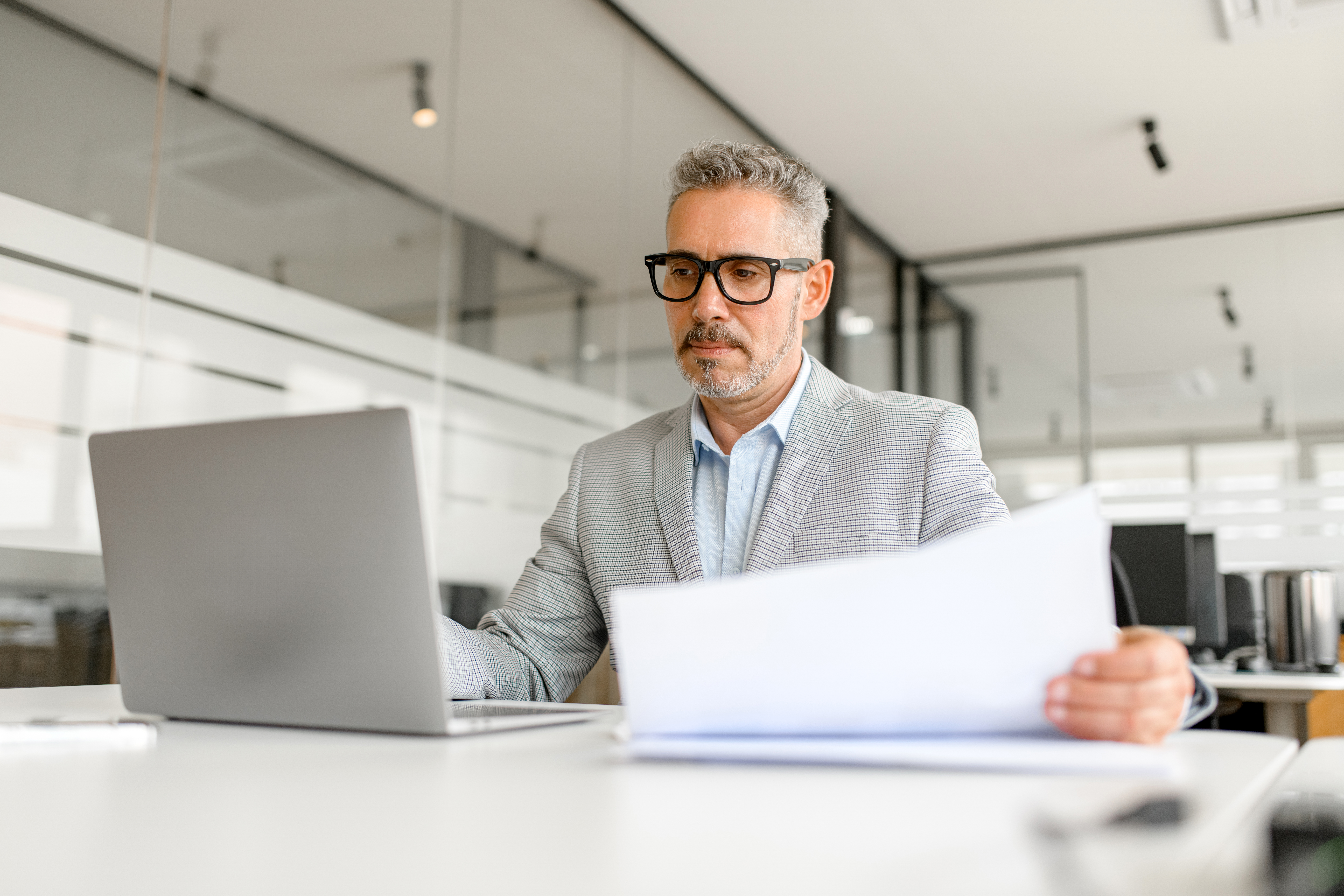 Business owner sitting at a desk with a laptop reviewing paperwork, determining the value of his business.
